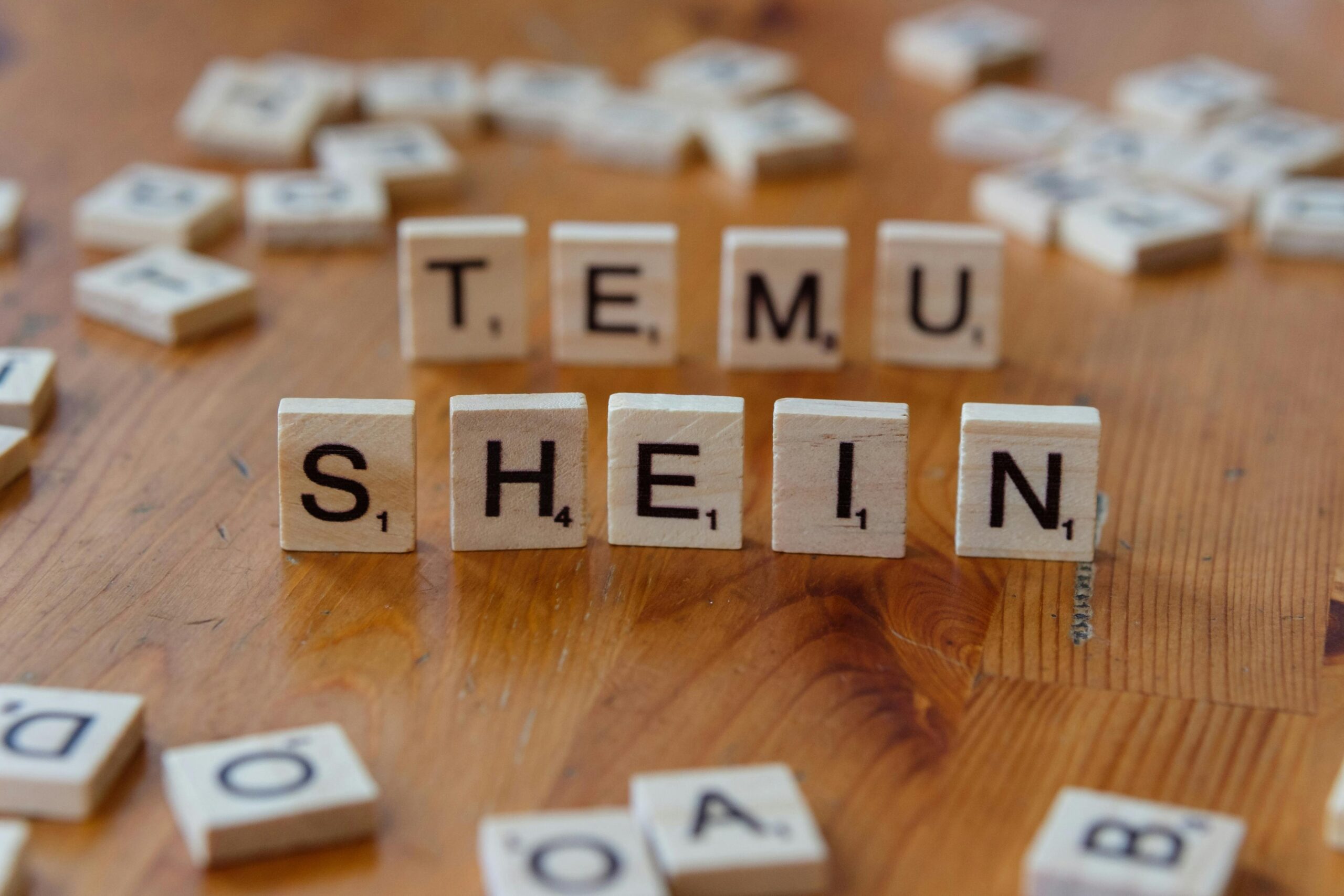 Scrabble tiles spelling 'TEMU SHEIN' on a wooden table, representing fashion brands.